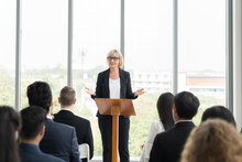 Senior Business Woman Talking At Podium Speaker. Senior Business Woman Wear Suit Standing Discussing Business Strategy Plan At Podium In Business Conference Room