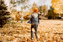 Kid Having Fun In Autumn Park With Fallen Leaves, Throwing Up Leaf. Child Boy Outdoors Playing With Maple Leaves