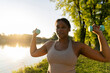 © gpointstudio - Plus sized African American woman exercising with dumbbells at the park in a  summer day