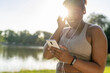 © gpointstudio - Plus sized African American woman using mobile phone and earphones before exercising at the park in a  summer day