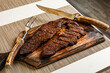 Ready to eat cooked grilled sliced piece of denver steak meat on wooden cutting board with cutlery