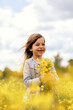 © mira_y - Little girl standing in a field with yellow flowers and laughing, holding a bouquet of wildflowers, flowers out of focus in the foreground, concept, peace, no war, peaceful sky, Ukraine