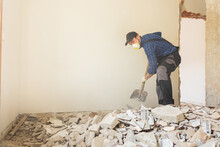 Busy Builder Collecting Construction Debris With A Shovel. Home Renovation Demolition Of Walls.