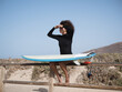 Young surfer female with afro hair watching the waves sitting on a fence