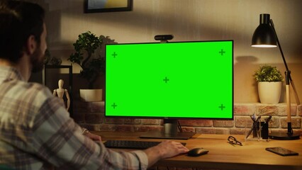 Fototapete - Office Employee Working from Home, Talking on Video Call on Desktop Computer with Monitor with Green Screen Mock Up. Man Sitting in Living Room, Chatting Online with Friends and Family in the Evening.