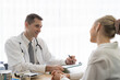 © amorn - Doctor and female patient. Male doctor discussing and writing note to seek advice problems with woman patient while sitting on the table in the office at the hospital