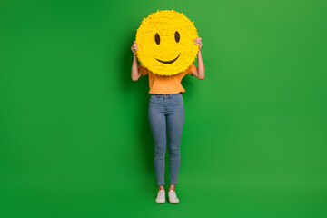 Canvas Print - Full body photo of excited carefree person hands hold large smile emoji cover face isolated on green color background