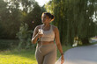 © gpointstudio - Plus sized African American woman using mobile phone and earphones during the walking at the park in a summer day