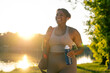 © gpointstudio - Young African American woman walking with bag and bottle of water through the park in a summer day