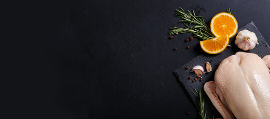 Raw and uncooked whole duck on slate board on black background