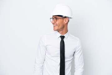 Young architect caucasian man with helmet and holding blueprints isolated on white background looking to the side and smiling