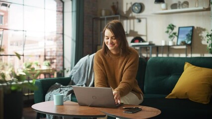 Poster - Smiling Young Woman Working from Home on Laptop Computer in Her Sunny Cozy Apartment, Relaxes and Leans Back on a Sofa. Successful Creative Female Entrepreneur Happy After Finishing Remote Work