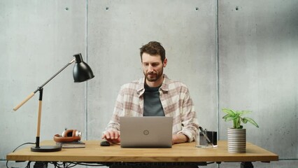 Poster - Professional Creative Man Sitting at His Desk in Office Working on a Laptop Computer. Stylish Clean Office Space Design Perfect for Productivity, Effectiveness and Vision. Medium Shot