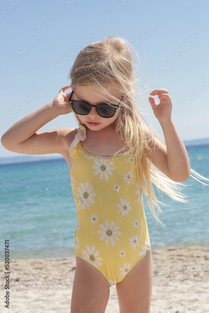 Portrait of 4 years old girl in yellow swimsuit and long blonde hair with blue sea and sky on the sandy beach Stock Photo Adobe Stock