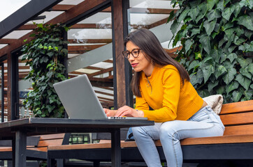 young, hispanic woman with indigenous features wearing a yellow sweater sitting on a bench outside w