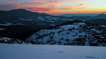 Wall Mural - Winter time lapse video with moving clouds over snow-covered mountain slopes and a small village nestled in them at sunrise, the Rhodopes in Bulgaria