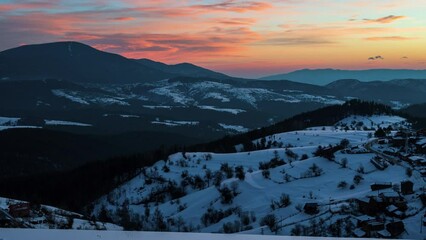 Wall Mural - Winter time lapse video with moving clouds over snow-covered mountain slopes and a small village nestled in them at sunrise, the Rhodopes in Bulgaria