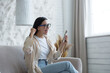 © Liubomir - Beautiful young brunette woman wearing glasses at home in living room shocked received good news, reading on phone and happy, celebrating victory, holding hand up success gesture