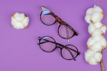 Wall Mural - Stylish women's glasses on a purple background with cotton flowers