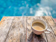 Cup of coffee on brown wooden table with defocus swimming pool or gradient blue blurry background