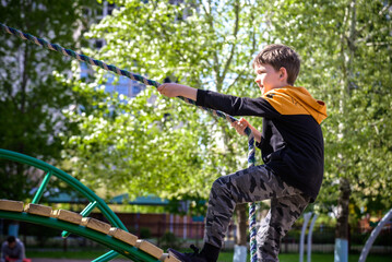 Wall Mural - Teenager boy climbing at kid playground outdoor. The climber trains simulator on the street. Healthy leisure for children concept