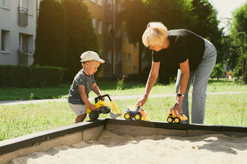 Wall Mural - Grandmother and child having fun together, playing in sandbox. Generation and childhood concept. Happy family symbol