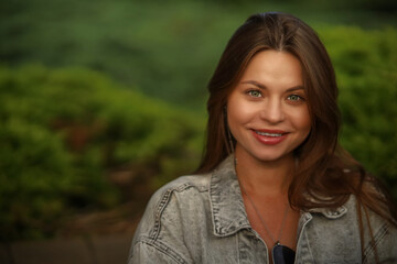 Wall Mural - Portrait of a pretty attractive sexy young woman with natural makeup with beautiful eyes in a fashionable denim jacket in a white stylish dress. American girl is walking around the park.