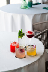 Poster - Four colorful summer cocktails in glasses on white table. Assortment of fresh summer drinks. Pink and red sangria cocktails, orange punch cocktail