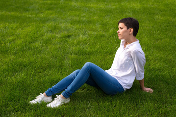 Wall Mural - Young woman sitting on the beautiful grass in spring