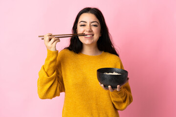 Wall Mural - Young caucasian woman isolated on pink background holding a bowl of noodles with chopsticks