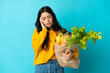 © luismolinero - Young woman holding a grocery shopping bag isolated on blue background with headache