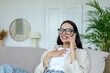 © Liubomir - Happy young woman at home sitting on sofa smiling and talking on the phone, brunette in glasses having fun having a free day