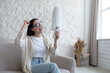 © Liubomir - Happy woman at home smiling and happy about received message, brunette sitting on sofa wearing glasses and holding phone in hand shouting cheerfully