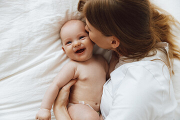 caring and loving mother kissing her little newborn daughter on the bed. mother playing with her baby in the bedroom