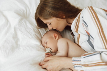 mother kissing her newborn baby sleeping on the bed at home. mother and baby are lying on the bed at home