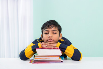 An indian boy fell asleep on the desk a lot of books