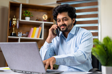 Happy businessman talking with client on mobile phone while working laptop at office - concept of consultation, financial advisor and white collar jobs.