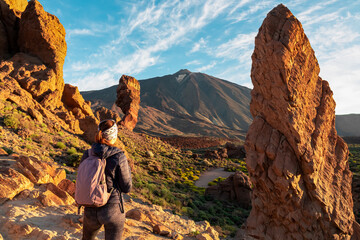 Woman with backpack hiking with scenic golden hour sunrise morning view on unique rock formation Roque Cinchado, Roques de Garcia, Tenerife, Canary Island, Spain, Europe. Pico del Teide volcano summit