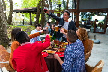 Young happy people having a barbecue dinner on a rooftop in patio - Group of friends having party and having fun – young people toasting in home terrace with beer glasses and wine glasses