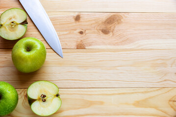 Flat lay photo of a few green apples one of wich sliced with a knife lying on a natural wooden background