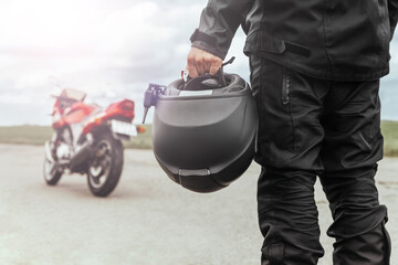 A man stands with his back to his motorcycle, holding a helmet