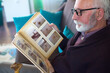 © Solid photos - Senior man looking at photos in photo album with photographs from his childhood