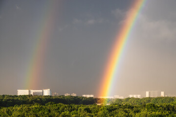 Sticker - double rainbow in gray sky over sunlit city park and apartment buildings before thunderstorm on sunny summer day