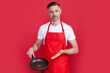 mature man chef in apron with frying pan on red background. presenting product