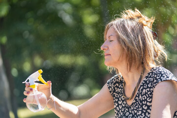 Mature woman curving herself in a public park with a water vaporizer in the middle of summer.