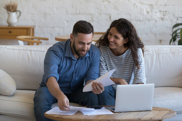 Wall Mural - Happy couple of 30s renters, homeowners doing domestic accounting job, household paperwork, reviewing paper documents at laptop computer, calculator, paying bills, mortgage, rent fees on internet