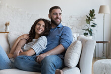 Cheerful Dreamy Young Dating Couple In Love Resting On Sofa, Relaxing At Home, Enjoying Leisure, Hugging, Looking Away, Planning Family Future, Marriage, Mortgage, Talking, Laughing