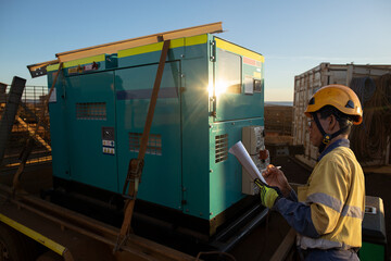 Construction worker wearing work uniform safety helmet conducting daily pre safety inspection checking on power generator unit prior used on construction building site, Australia 
