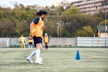 Wall Mural - Athletic woman leading ball around cones on soccer training at stadium.