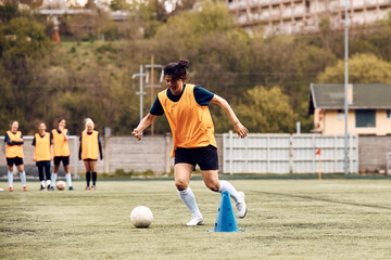 Wall Mural - Female soccer player dribbling ball around cones during sports training.